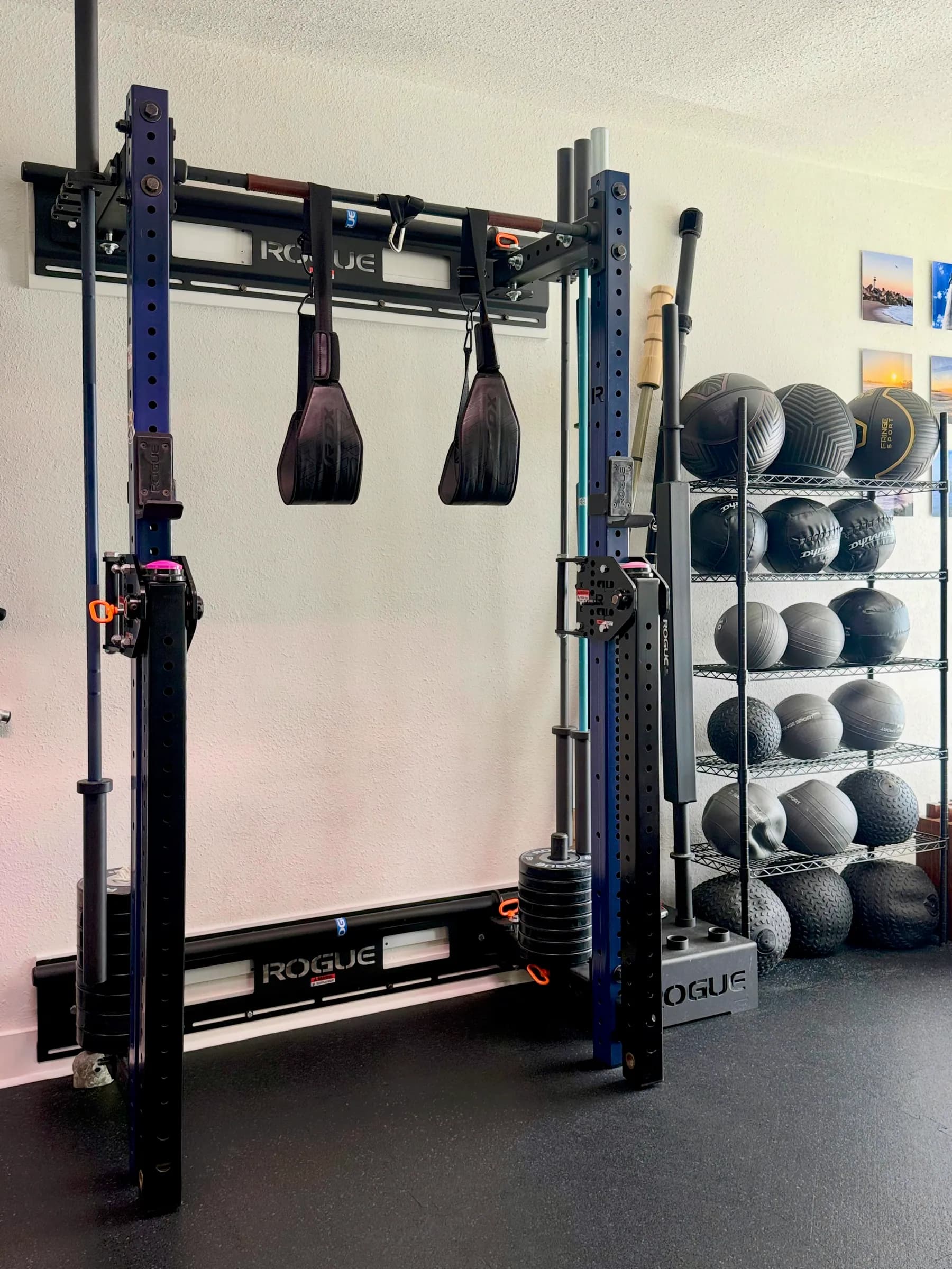 Rogue wall rack with rings, a barbell, and a shelf of slam balls and medicine balls at Mavericks Fitness